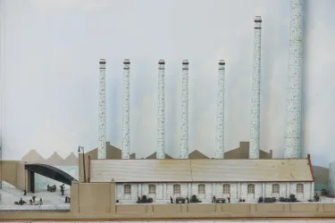 Ein detailliertes Modell einer Fabrik mit mehreren Schornsteinen. Die Szene zeigt Arbeitern und verschiedenen Gebäuden.