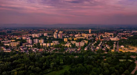 Eine Stadtansicht mit Wohngebäuden und grünen Flächen. Der Himmel zeigt einen schönen Farbverlauf bei Sonnenuntergang.