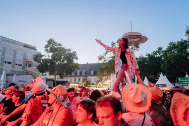 Eine lebhafte Menschenmenge bei einem Fest. Eine Frau steht auf den Schultern anderer und genießt die Atmosphäre.