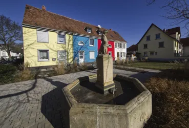 Ein schöner Platz mit bunten Häusern und einem Brunnen in der Mitte. Die Architektur ist modern und die Umgebung ist gepflegt.