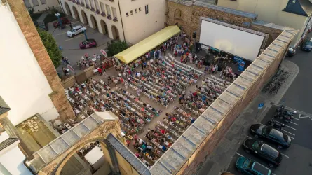 Ein Freiluftkino mit vielen Stühlen und einer großen Leinwand. Eine große Menschenmenge versammelt sich, um einen Film zu sehen.