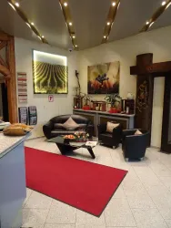 Ein einladender Eingangsbereich mit einer modernen Sitzgruppe und einem roten Teppich. An den Wänden hängen Bilder von Weinreben und Trauben.