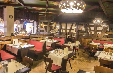 Ein gemütliches Restaurant mit Holzmöbeln und warmem Licht. Die Tische sind mit weißen Tischdecken und Besteck gedeckt.