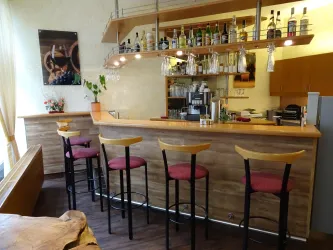 Ein gemütlicher Barbereich mit hölzernem Tresen und Stühlen. Die Regale sind mit verschiedenen Getränken dekoriert, und die Atmosphäre wirkt einladend.