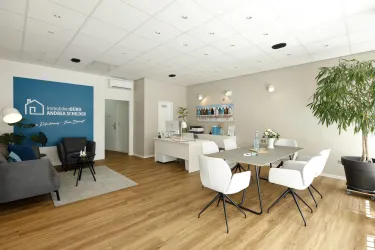Ein modernes Büro mit einem Empfangsbereich und einem großen Tisch. Es gibt helle Möbel, Pflanzen und eine dekorative Wand in Blau.