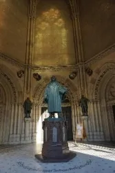 Eine Statue von Martin Luther steht im Zentrum eines gotischen Raumes. Helle Lichtstrahlen fallen durch die Fenster und schaffen eine beeindruckende Atmosphäre.