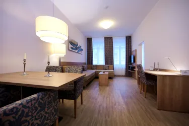 Ein modernes Wohnzimmer mit einem gemütlichen Sofa und einem Esstisch. Große Fenster sorgen für viel Tageslicht. Das Sofa besteht aus 2 Boxspringbetten und istideal geeignet als Bett (je 90x200cm) für die 3. und 4. Person.