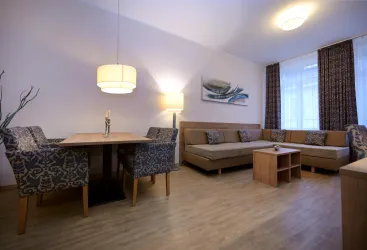 Ein modernes Wohnzimmer mit einem gemütlichen Sofa, einem Esstisch und stilvollen Stühlen. Große Fenster sorgen für viel natürliches Licht.