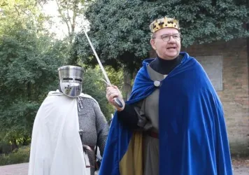 Ein König in einem blauen Umhang hält ein Schwert und spricht. Neben ihm steht ein Ritter in einer Rüstung und mit einem Helm.