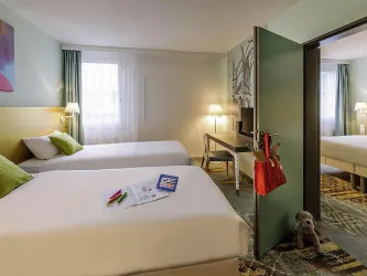 Ein modernes Hotelzimmer mit zwei Einzelbetten und einem Schreibtisch. Die Wände sind in angenehmen Farben und es gibt viel Tageslicht durch die Fenster.