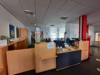 Ein modernes Empfangsgebiet mit Holzregalen und einem dunklen Empfangstresen. Im Hintergrund sind Schreibtische und Bürostühle zu sehen.