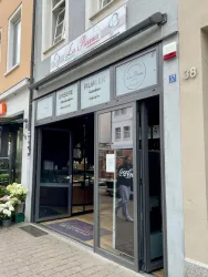Ein kleines Café namens "La Panna" mit großen Glasfronten. Draußen stehen Blumen und der Eingang ist einladend gestaltet.