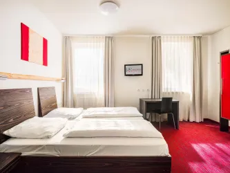 Ein modernes Schlafzimmer mit einem Doppelbett und einem kleinen Schreibtisch. Die Wände sind hell, und große Fenster lassen viel Licht herein.