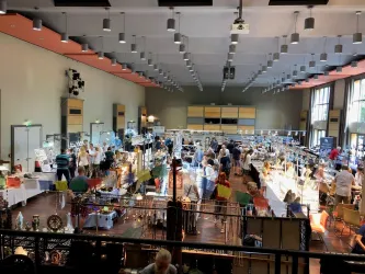 Ein lebhafter Markt mit zahlreichen Ständen und Menschen. Die Ausstellung bietet eine Vielzahl von Waren in einem hellen, freundlichen Raum.