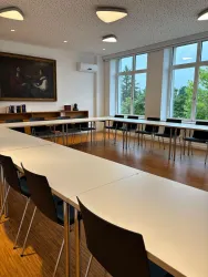 Ein moderner Konferenzraum mit einem langen Tisch und Stühlen. Große Fenster bieten einen Blick ins Grüne.