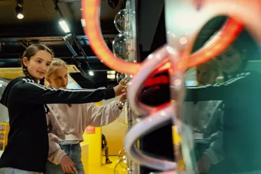 Zwei Mädchen interagieren mit einer Ausstellung in einem modernen Museum. Sie scheinen interessiert und neugierig zu sein.