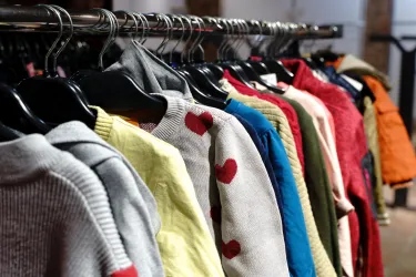 Eine Auswahl an bunten Pullovern hängt an Verkaufsständern. Die Kleidungsstücke sind in verschiedenen Farben und mit unterschiedlichen Mustern gestaltet.