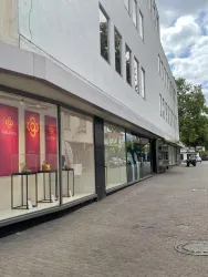 Ein modernes Geschäftshaus mit großen Fenstern und einem einladenden Eingang. Die Fassade ist schlicht und die Umgebung wirkt freundlich und hell.