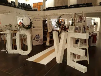 Eine dekorative Art von den Buchstaben "LOVE" aus Holzelementen. Im Hintergrund sind weitere Dekorationen und Stände für eine Veranstaltung zu sehen.