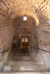 Eine steinerne Treppe führt hinunter in einen alten, gemauerten Raum. Am Ende der Treppe ist ein Fenster, das Licht hereinlässt.