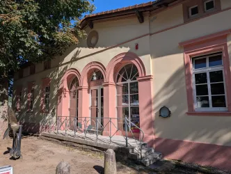 Ein historisches Gebäude mit einer schönen Fassade in sanften Farben. Die große Fensterfront und der Balkon verleihen dem Bauwerk eine einladende Note.