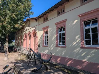 Ein historisches Gebäude mit roten Akzenten und großen Fenstern. Im Vordergrund befindet sich eine moderne Skulptur.