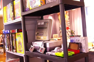 Ein Regal mit verschiedenen Videospielen und Konsolen. Im Vordergrund sind eine Super Nintendo Konsole und ein Game Boy sichtbar.