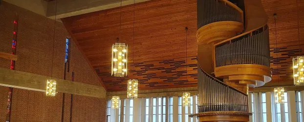 Ein moderner Innenraum mit einer beeindruckenden Holzdecke und einer spiralförmigen Treppe. Leuchtende Pendelleuchten ergänzen das elegante Design.