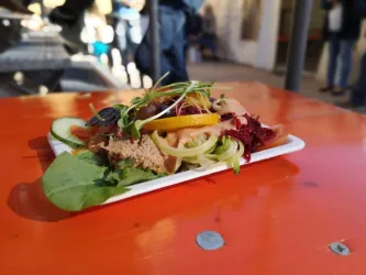 Ein Teller mit frischem Salat, der auf einem orangefarbenen Tisch steht. Der Salat enthält verschiedene Gemüsesorten und ist mit Kräutern garniert.