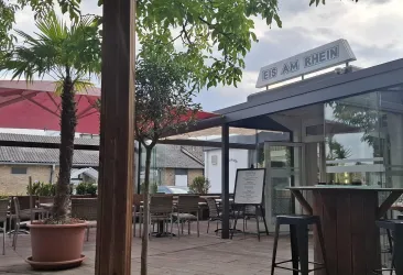 Ein einladendes Restaurant im Freien mit Palmen und Tischen. Der Himmel ist bewölkt, und die Atmosphäre ist gemütlich.
