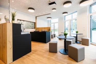 Eine moderne Café-Umgebung mit Holzelementen und stilvollen Möbeln. Große Fenster sorgen für viel Tageslicht und eine einladende Atmosphäre.