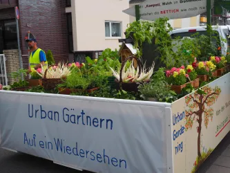 Ein Wagen mit vielen verschiedenen Pflanzen und Kräutern steht auf der Straße. Darauf steht der Schriftzug "Urban Gärtnern" und es gibt eine dekorative Baumgrafik.