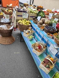 Ein farbenfroher Marktstand mit frischen Obst- und Gemüsekörben. Die Tische sind mit einer Vielzahl von Produkten wie Äpfeln, Birnen und Kartoffeln dekoriert.