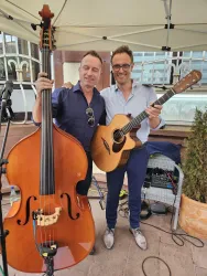 Zwei Musiker stehen zusammen unter einem Zelt. Der eine hält einen Kontrabass, der andere eine Gitarre und beide lächeln in die Kamera.