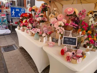 Ein bunter Stand mit vielen kunstvollen Papierblumen in verschiedenen Farben. An einer Tafel steht der Schriftzug „Alles aus Papier“.