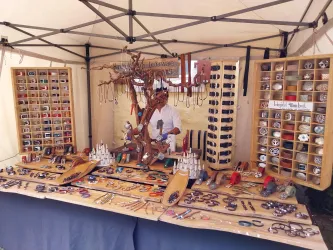 Ein Schmuckstand mit handgefertigten Anhängern, Ketten und anderen Accessoires. Eine Person arbeitet an einem Tisch voller dekorativer Stücke.