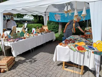 Ein Marktstand mit verschiedenen handgefertigten Töpferwaren und Kunsthandwerk. Eine Person steht am Tisch und betrachtet die angebotenen Artikel.