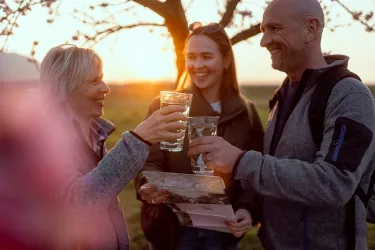 Drei Personen stehen Draußen unter einem Mandelbaum und stoßen mit Weingläsern an