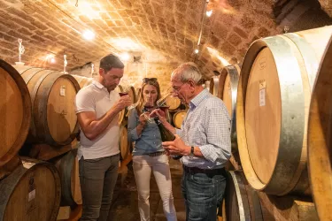 Drei Menschen stehen in einem Weinkeller, von Weinfässern umgeben und riechen an mit Wein gefüllten Gläsern