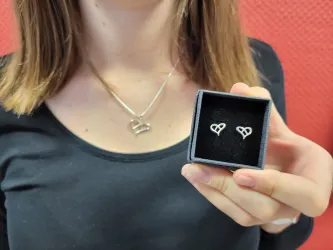 Eine Frau trägt eine Kette mit einem brezelförmigen Anhänger und zeigt zwei Ohrstecker ebenso in Brezelform in die Kamera