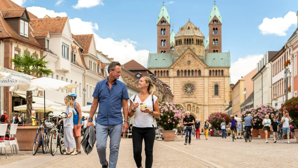 Zwei Personen laufen durch belebte Innenstadt, im Hintergrund der Dom zu Speyer