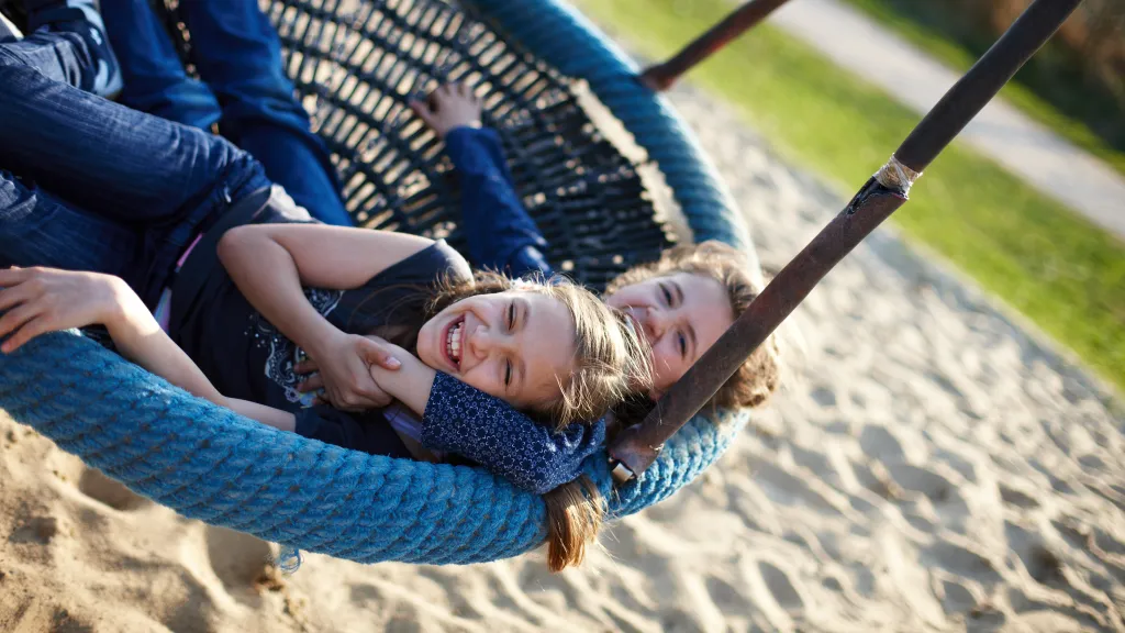 Zwei Personen in einer Korbschaukel auf einem Spielplatz