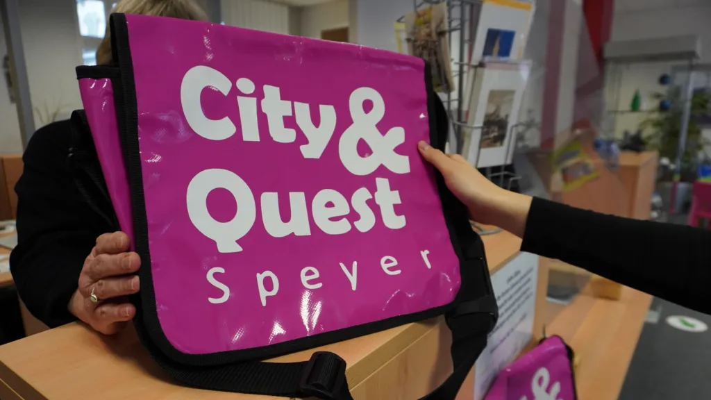 Eine pinke Tasche mit der Aufschrift "City & Quest Speyer) steht auf einem Counter
