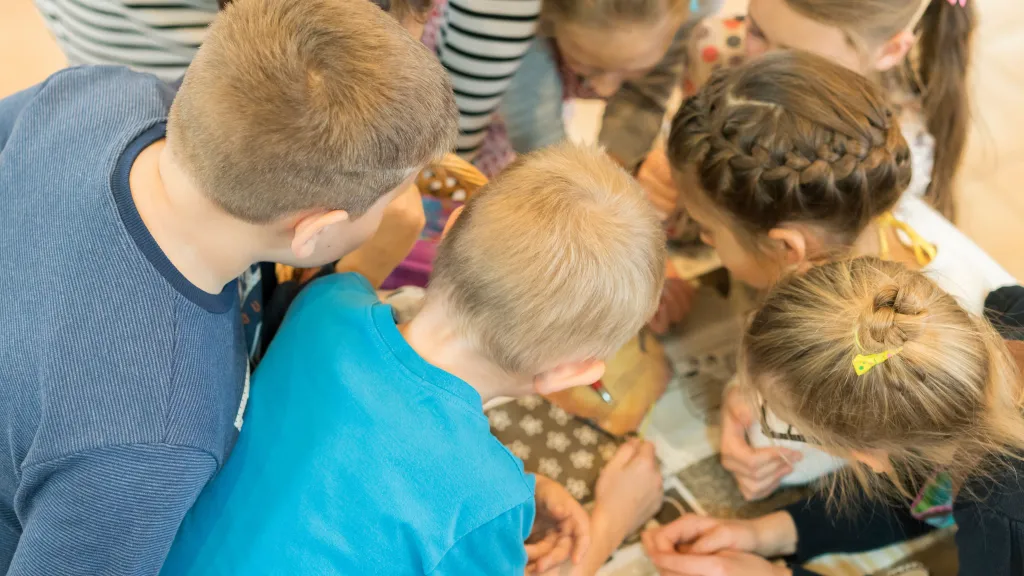Viele Kinder stecken die Köpfe über einem Tisch zusammen 