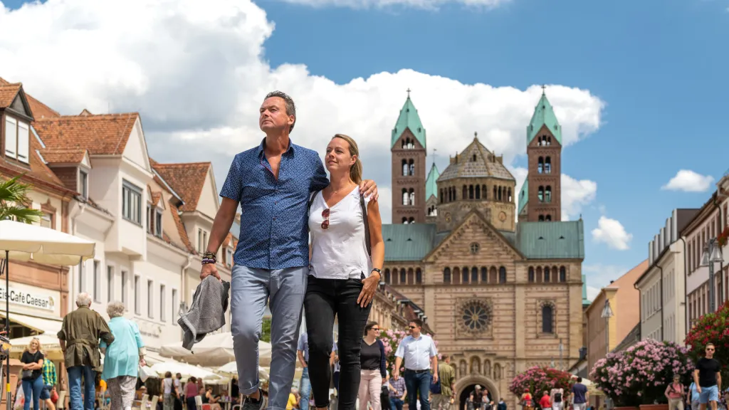 Zwei Personen laufen auf einer belebten Straße, im Hintergrund ist der Speyerer Dom zu sehen