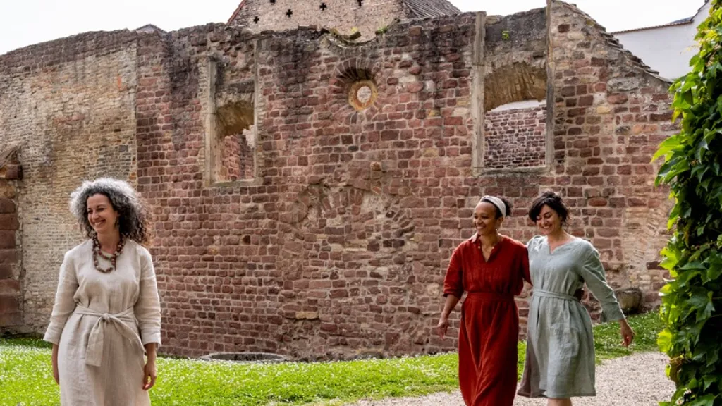 Drei Frauen laufen in Gewändern durch den Judenhof in Speyer
