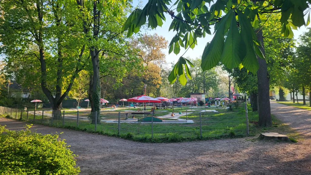 Grüne Bäume und Büsche, ein Weg aus feinen Kieselsteinen und im Fokus eine Minigolfanlage
