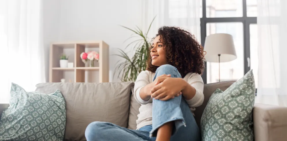 Eine Frau sitzt mit einem angewinkelten Bein auf einem Sofa