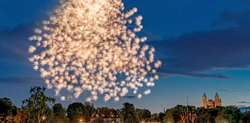 Rhein bei Dunkelheit mit einem Schiff, rechts ist der Dom zu sehen und in der Mitte ein prächtiges goldenes Feuerwerk