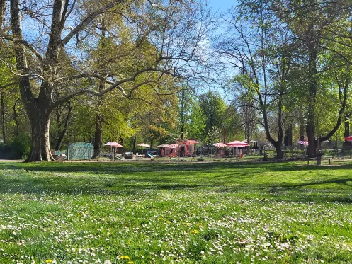 Grüne Wiese und Bäume umrahmen das Bild, in der Mitte ist in der Ferne eine Minigolf-Anlage zu erkennen